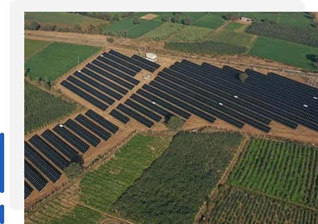 Aerial drone view of a large ground-mounted solar power plant with multiple rows of photovoltaic panels installed across agricultural land, showcasing a utility-scale solar energy farm in a rural landscape